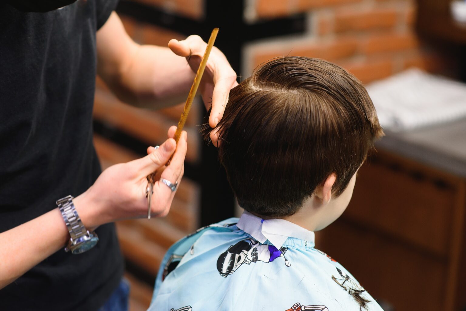 A little cute boy sits in a hairdresser's at the stylist's, a schoolchild is getting hair cut in a beauty salon, a child at a barbershop's, a short men's haircut.